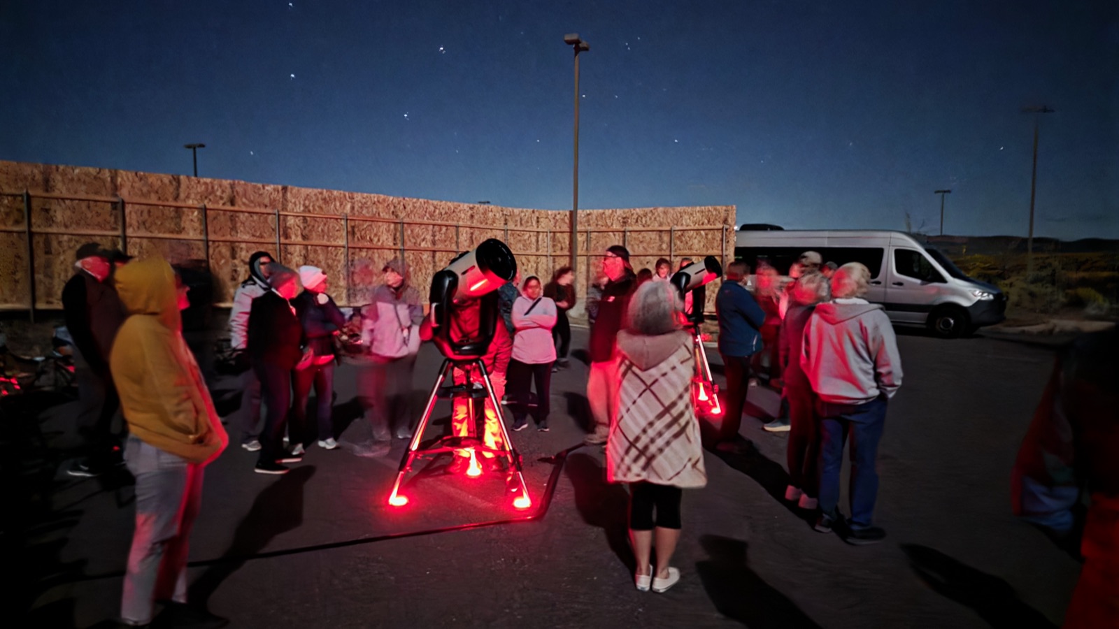Small tour group gathered around a telescope beside the tour van at night near Bryce Canyon